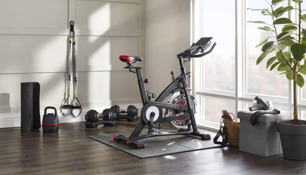 Un vélo d'exercice, des haltères, des accessoires et un cube de rangement dans le coin d'une pièce de la copropriété.