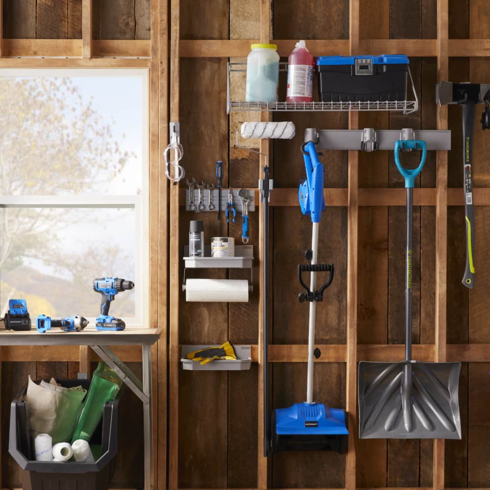 An unfinished shed wall with the MOD™ system being used to hold tools, shovels, and a rack for a small toolbox and two plastic jugs.