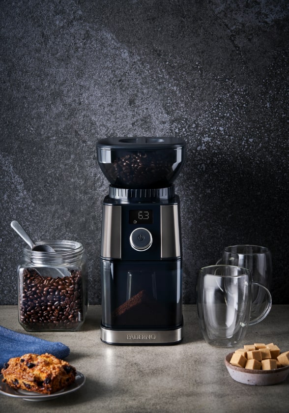 PADERNO Burr Coffee Grinder with a jar of coffee beans, glass mugs, and pastries on the side