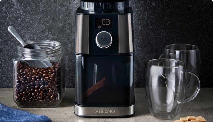 Moulin à café PADERNO avec un contenant de grains de café, des tasses en verre et des pâtisseries à côté