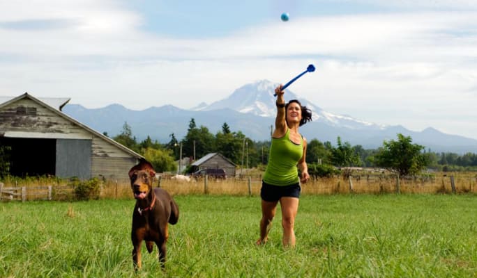 Une femme dans un champ utilisant un lanceur de balle avec un chien 