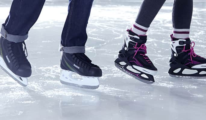Two individuals wearing rec skates on ice.