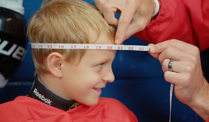 Un entraîneur mesurant la tête d'un joueur de hockey avec un ruban à mesurer.