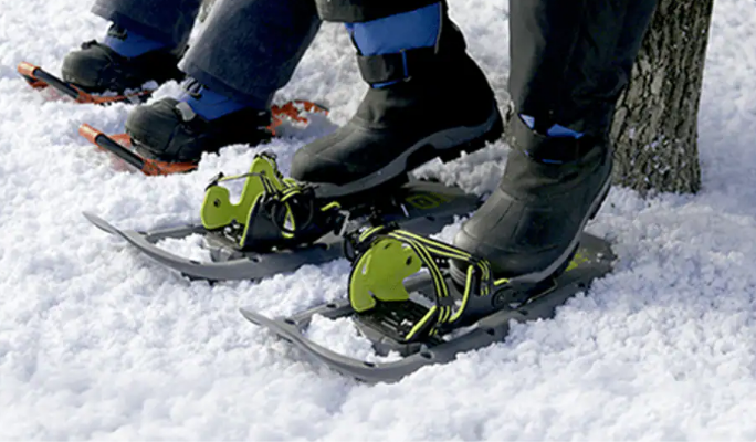 Two people wearing Outbound snowshoes in wintery woods area.