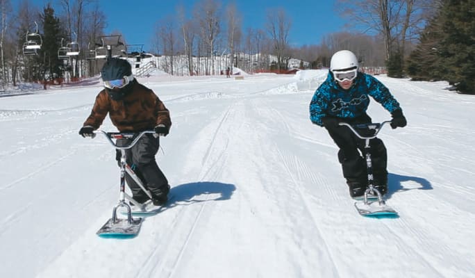 Two individuals snow racing downhill in woodsy area.