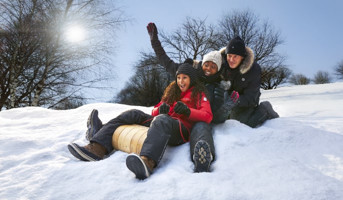 Three individuals sliding down snow hill with toboggan. 