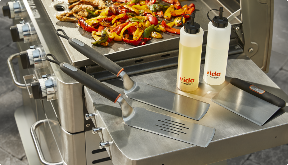 Outils de cuisson Vida par PADERNO et bouteilles compressibles sur le panneau latéral d’un barbecue.
