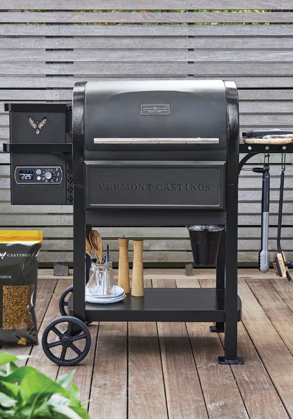 Vermont Casting Woodland Pellet Grill on backyard patio with cooking accessories. 
