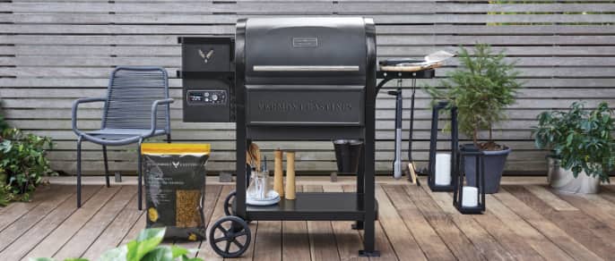 Vermont Casting Woodland Pellet Grill on backyard patio with cooking accessories. 