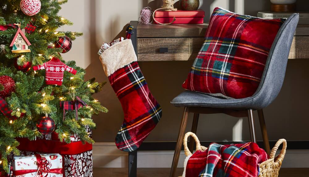 Plaid stocking handing on a desk and a plaid pillow on chair next to a Christmas tree