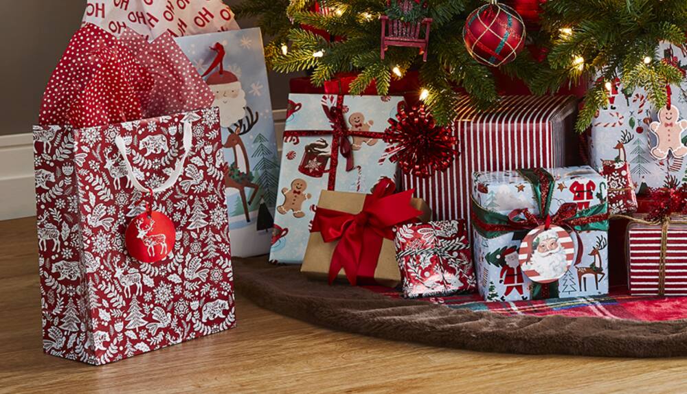 Cadeaux enveloppés avec les articles d’emballage de la collection CANVAS rouge, posés sous un arbre