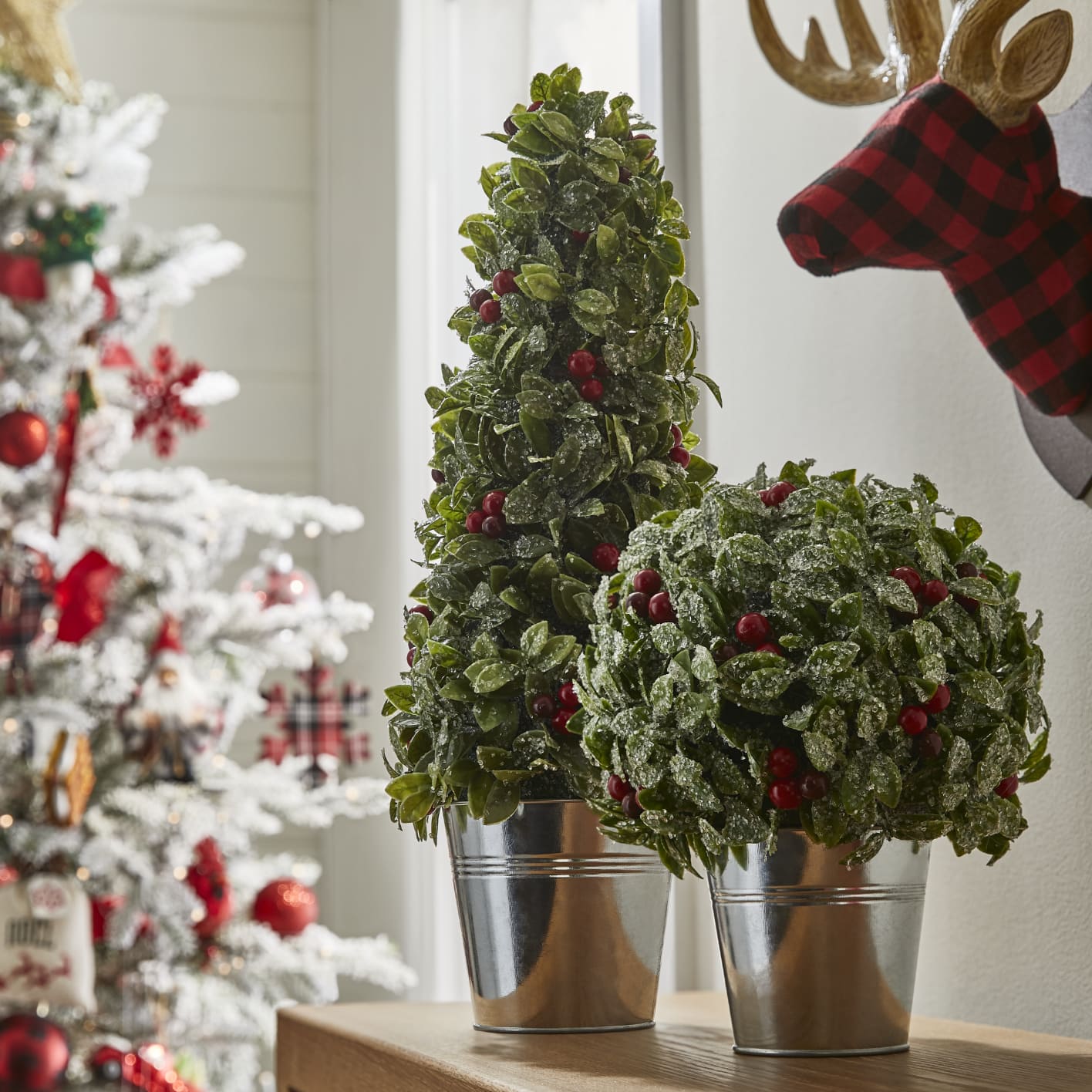 Two small CANVAS tabletop holly trees placed on a shelf.