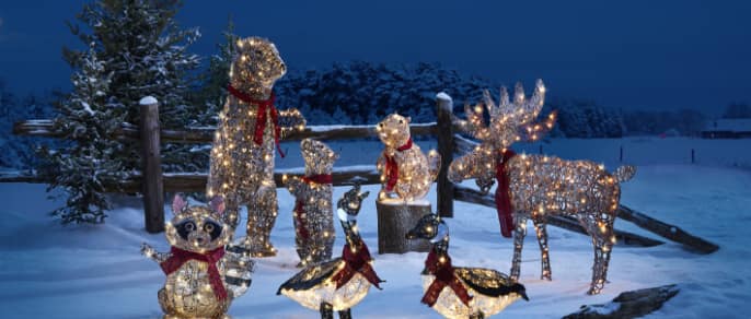 CANVAS Canadian Cabin bear, moose, and geese Christmas figures lit up on a snowy lawn.