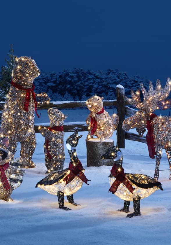 CANVAS Canadian Cabin bear, moose, and geese Christmas figures lit up on a snowy lawn.