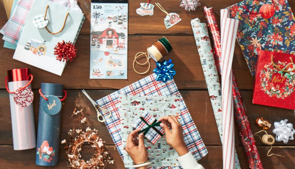 Colourful table spread of CANVAS Countryside Christmas wrapping paper, gift bags, and wrapping accessories.