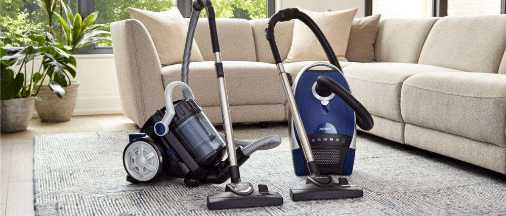 Two canister vacuums on a decorative rug in a bright, airy living room.
