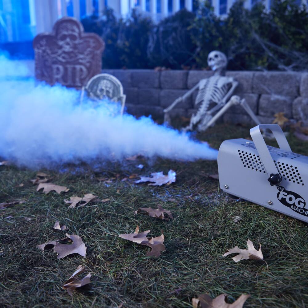 Scary Halloween porch decor with hanging ghost, lit up pumpkins, headstones and fog.