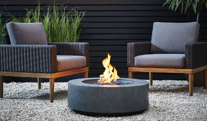 Two outdoor club chairs arranged around a CANVAS Erikson Gas Fire Table on a patio.
