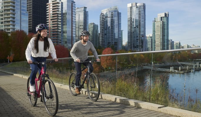 Un couple faisant du vélo le long d’un paysage urbain et d’une étendue d’eau. 