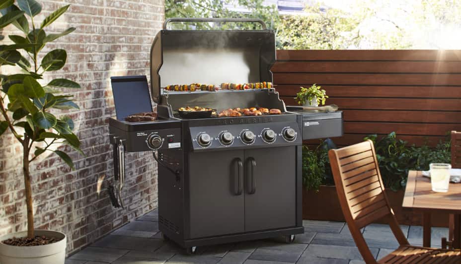 Coleman Pro 5-Burner Convertible Grill in backyard, grilling skewers and meat.