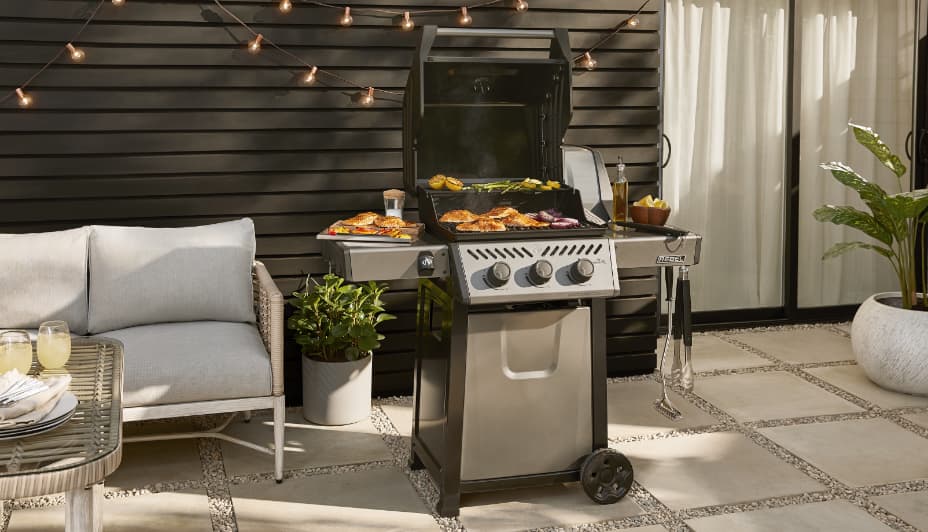 Napoleon Rebel 3-Burner Propane Grill in backyard, grilling meat and veggies. 