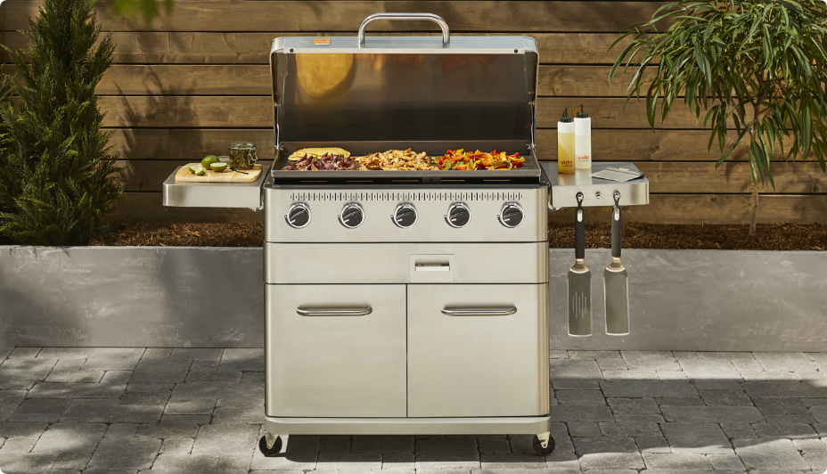 Vida by PADERNO 5-Burner Griddle in backyard grilling meat and skewers. 