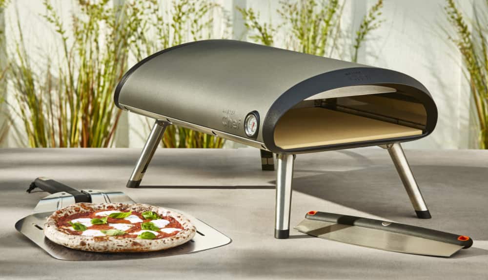 Cooked pizza and MASTER Chef Gas Pizza Oven on patio table. 