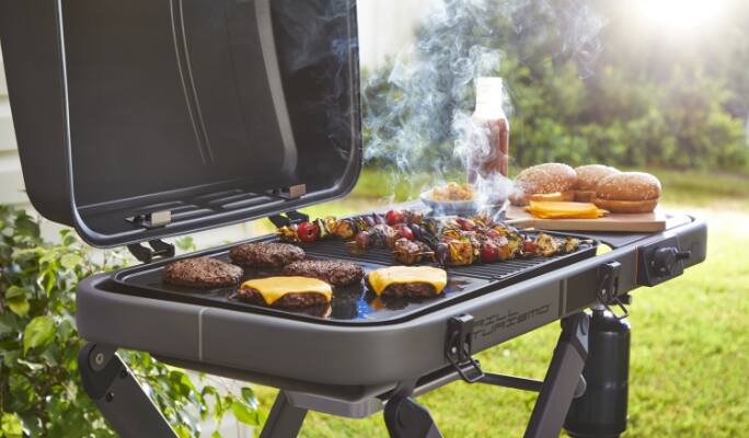 Cast iron grill cooking burgers and skewers in backyard. 