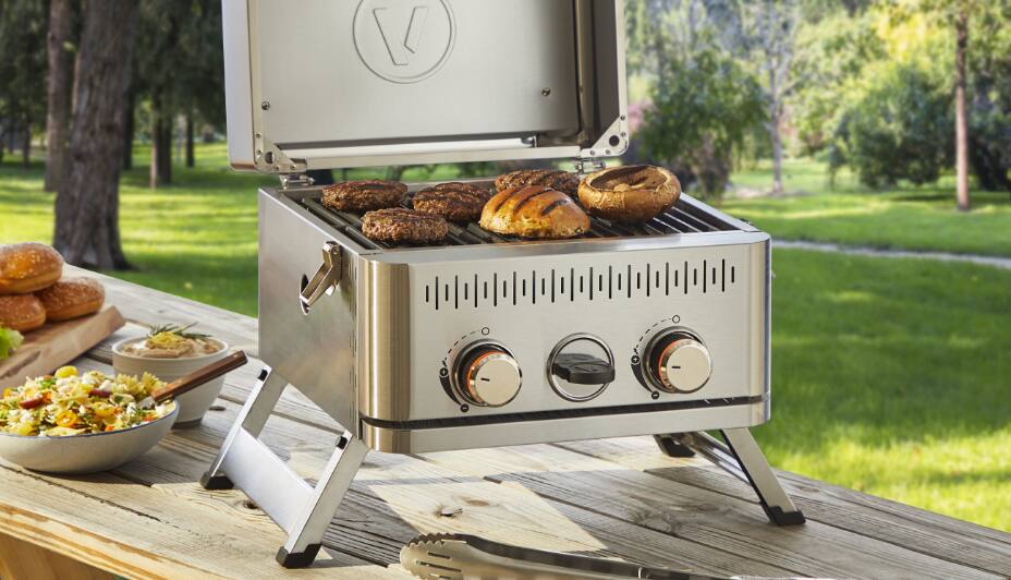 Vida by PADERNO Portable Gas Grill on park picnic table, grilling burgers and buns.  