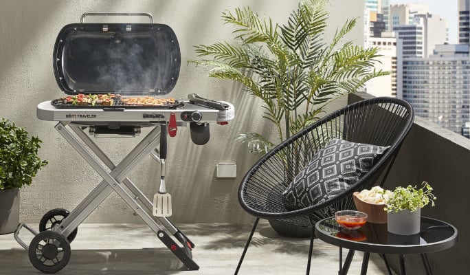 Weber Traveler Portable Propane BBQ open on balcony, grilling veggies.