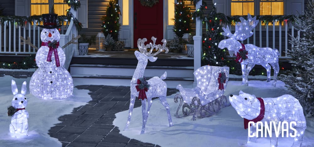 Collection of CANVAS Arctic white wireform lawn decorations including a moose, pair of snowmen and a polar bear lit up at night in front of a home.