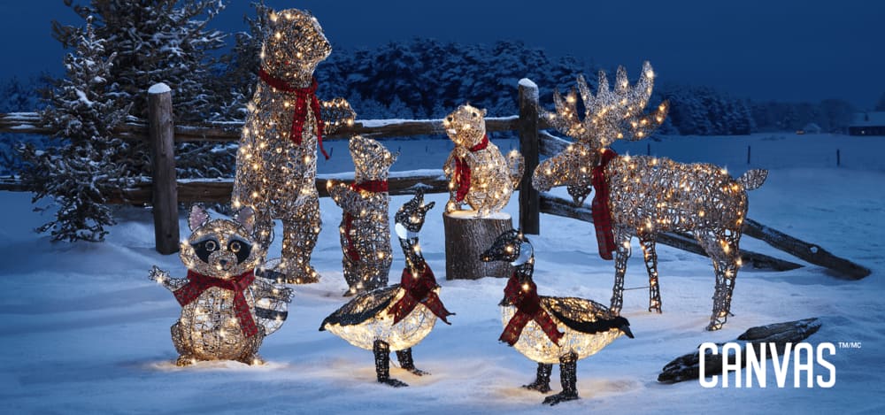Une collection de figures en fil métallique illuminées, dont des ours, un castor, des oies et un orignal CANVAS chalet canadien groupés ensemble avec un arrière-plan enneigné.