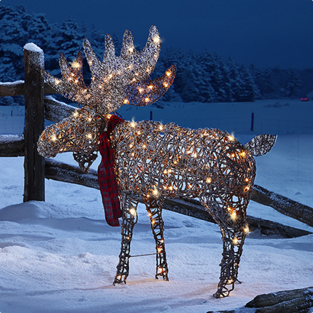 A moose wireform figure lit up on a snowy lawn.