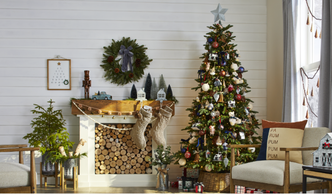 Des décorations de Noël dans un salon à ambiance d’auberge avec un foyer, comprenant un arbre de Noël, une couronne, des bas et des accessoires en nouveauté.