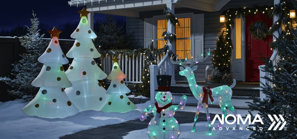 Sapins de Noël, bonhomme de neige et cerf intelligents NOMA Advanced 2.0 illuminés devant une maison sur une pelouse enneigée.