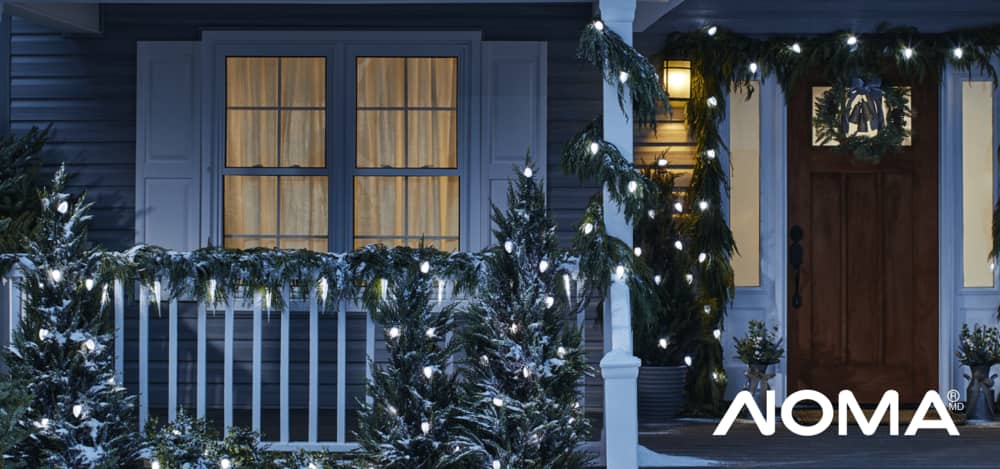 Jeu de lumières de Noël lueur boréale NOMA qui illumine un porche et des arbres à l’extérieur d’une maison.