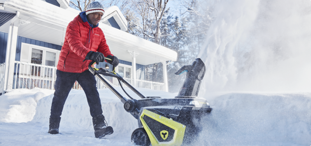 A man uses a Yardworks 97V Single Stage Cordless Snowblower to clear a snowy driveway.