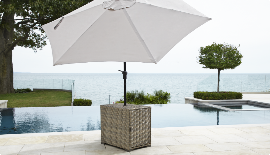 Table de jardin pour parasol CANVAS Bala exposée sur une terrasse au bord de la piscine avec un parasol blanc. 