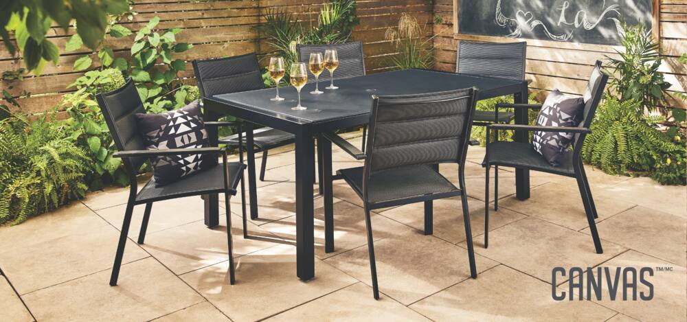A black furniture set that includes a large outdoor table and six chairs, with four glasses of white wine placed on the table.