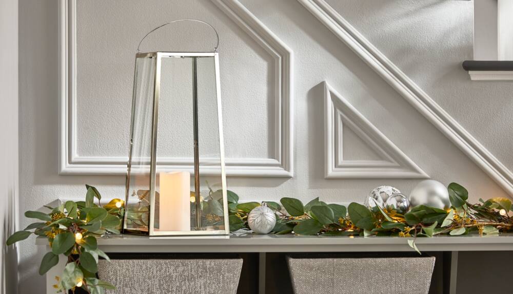 CANVAS 18-in Silver Lantern on a table with a lit-up Silver Eucalyptus Garland.