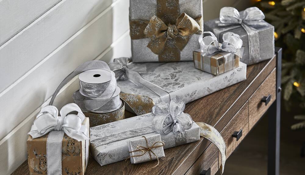 Wrapped gifts and ribbons from the CANVAS Silver Wrapping Paper Collection on an entryway table.