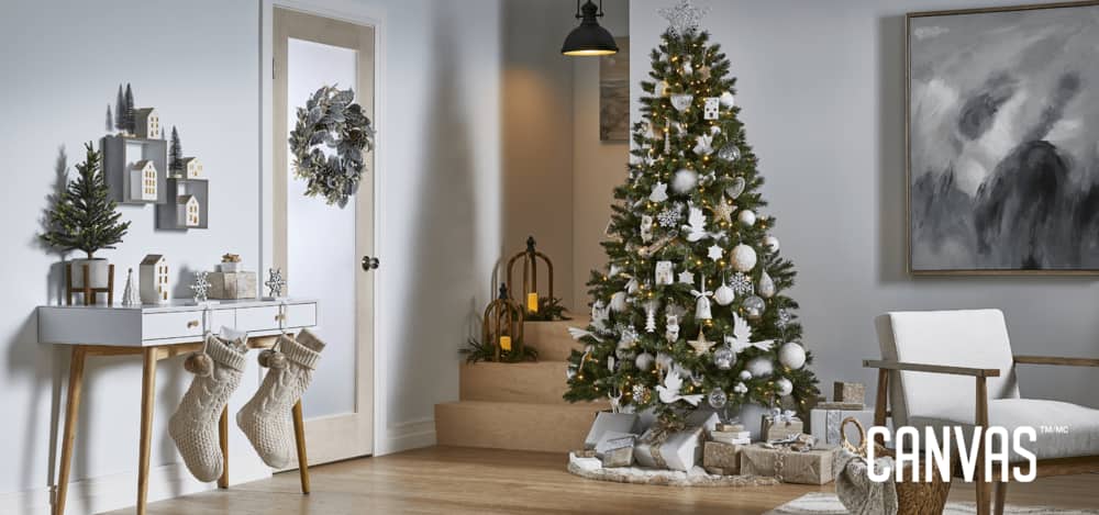 A room in a modern home decorated with CANVAS White Christmas decorations, including stockings, a wreath, a potted tree, and a Christmas tree decorated with ornaments.