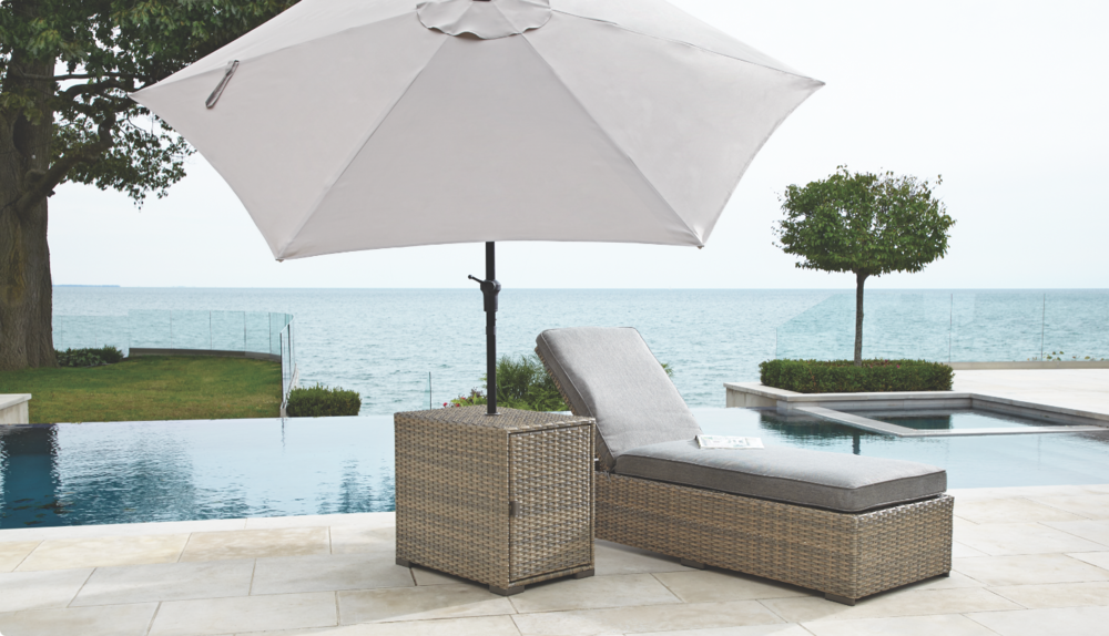 Une chaise longue de jardin et un parasol au bord d’une piscine. 