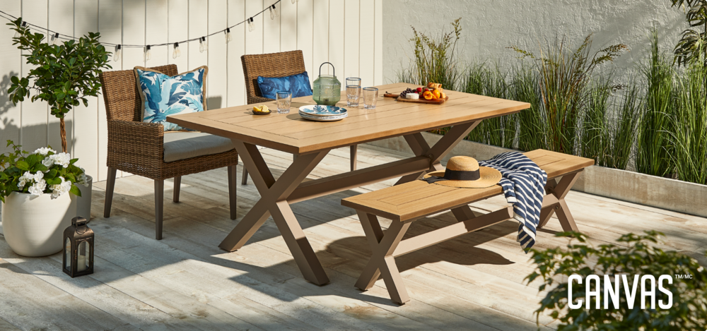  CANVAS Belwood Collection in wooden backyard porch dining area featuring wicker woven armchairs with cushioning and pillows, wooden dining table, and wooden dining bench.