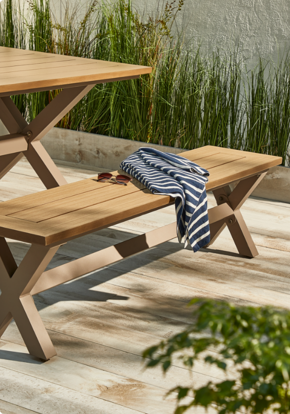  CANVAS Belwood Dining Bench on wooden backyard porch dining area featuring wood accents, sunglasses and stripped scarf on the bench.