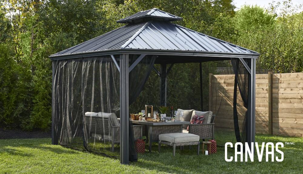 CANVAS Skyline Gazebo set up in a backyard grassed patio with lounge chairs, table and bug netting. 