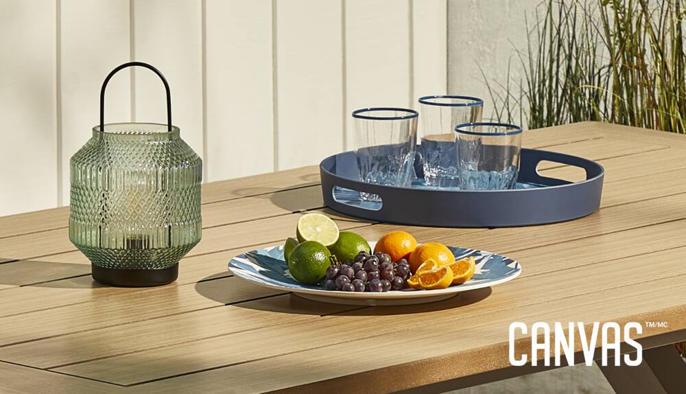 CANVAS Summer Palm Dinnerware Collection on CANVAS Bellwood Patio Table featuring decorative lantern, 3 glasses on tray and platter with fruit on top.