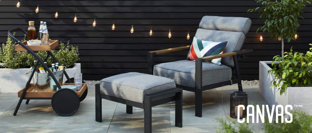 CANVAS Casell Recliner Chair in backyard patio featuring plush cushioning and ottoman, alongside a wood-like bar cart, outdoor plants and decorative string lights. 