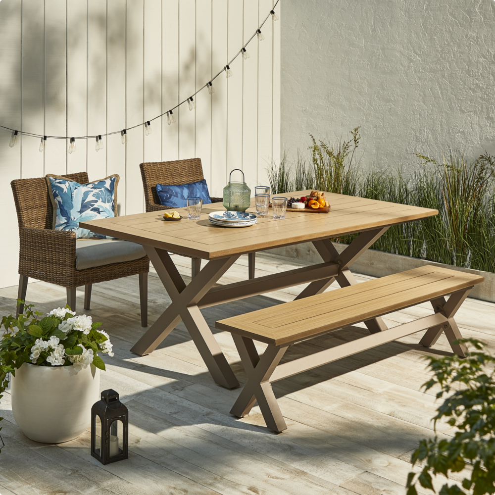 CANVAS Belwood Dining Collection set up on patio with two wicker chairs, wooden table and bench.