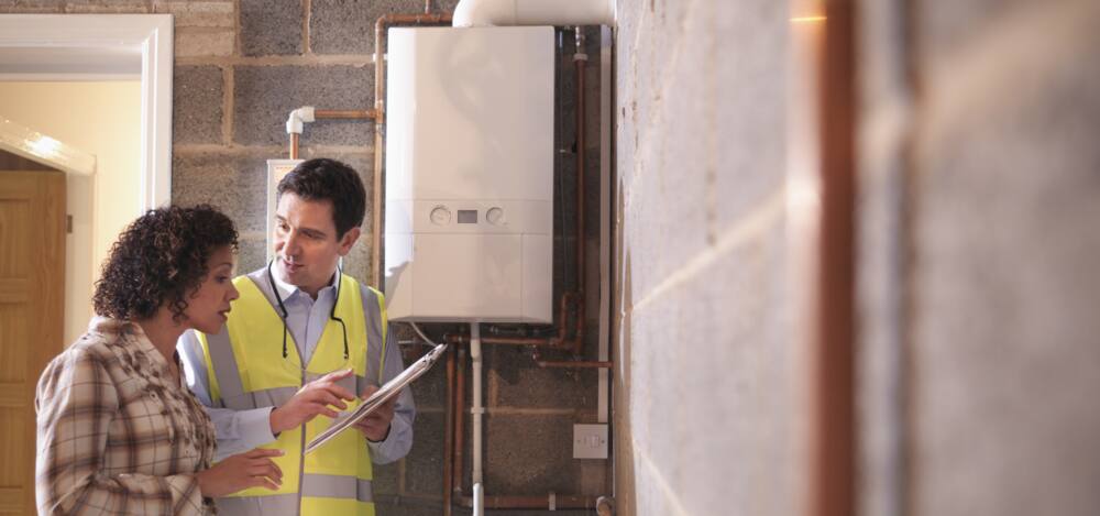 A technician with a clipboard speaks to a homeowner in front of an electric tankless water heater.